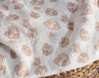 May include: White fabric with a repeating pattern of brown tropical leaves. The fabric is draped over a woven basket, creating a textured and layered effect. The leaves are detailed with outlines and filled with a lighter brown color.