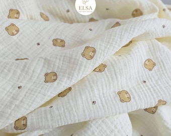 May include: Cream-colored muslin fabric with a repeating pattern of brown teddy bear faces and small paw prints. The fabric is soft and textured, with visible folds and wrinkles. The logo "ELSA COTTON HOUSE" is visible in the upper right corner.