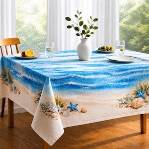 May include: A round tablecloth featuring a beach scene with blue waves, sand, and starfish. The tablecloth is on a wooden table with a vase of greenery and a plate of fruit. The overall color scheme is blue, beige, and white.