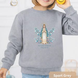 May include: Sport grey sweatshirt featuring an illustration of Our Lady of Fatima with the text "Our Lady of Fatima Pray for Us." The design includes floral and leaf accents in shades of blue and green.