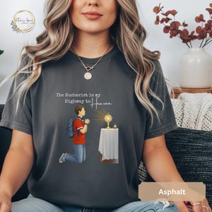Unisex Bella and Canvas Catholic t-shirt featuring Saint Carlo Acutis kneeling in Eucharistic Adoration with the quote “The Eucharist is my Highway to Heaven,” Christian faith apparel for men and women. Perfect for Catholic gifts.