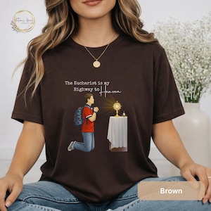 Unisex Bella and Canvas Catholic t-shirt featuring Saint Carlo Acutis kneeling in Eucharistic Adoration with the quote “The Eucharist is my Highway to Heaven,” Christian faith apparel for men and women. Perfect for Catholic gifts.