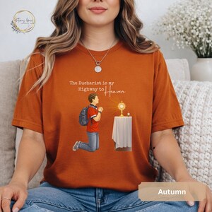 Unisex Bella and Canvas Catholic t-shirt featuring Saint Carlo Acutis kneeling in Eucharistic Adoration with the quote “The Eucharist is my Highway to Heaven,” Christian faith apparel for men and women. Perfect for Catholic gifts.