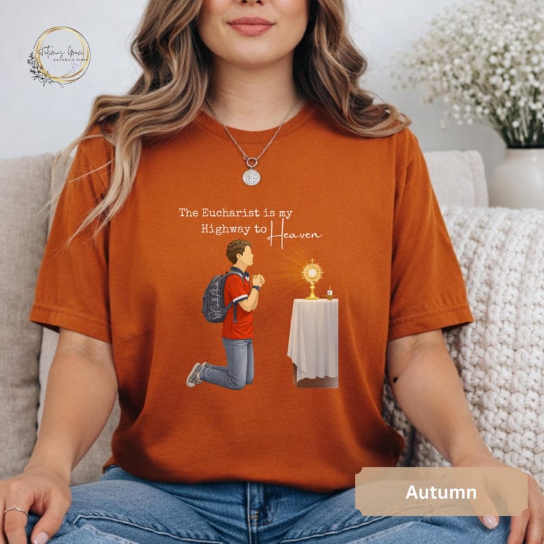 Unisex Bella and Canvas Catholic t-shirt featuring Saint Carlo Acutis kneeling in Eucharistic Adoration with the quote “The Eucharist is my Highway to Heaven,” Christian faith apparel for men and women. Perfect for Catholic gifts.