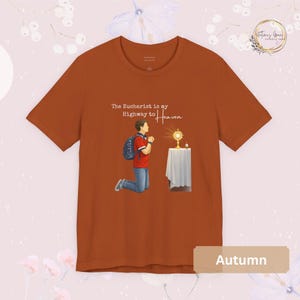 Unisex Bella and Canvas Catholic t-shirt featuring Saint Carlo Acutis kneeling in Eucharistic Adoration with the quote “The Eucharist is my Highway to Heaven,” Christian faith apparel for men and women. Perfect for Catholic gifts.