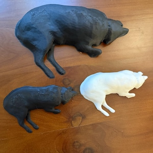 May include: Three 3D-printed bear figurines in black and white. The largest bear is black, and the other two are smaller, with one black and one white. All are lying down, with their legs extended.