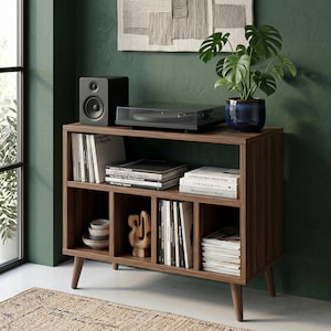 May include: A dark wood media console with four tapered legs, featuring an open top shelf holding a black speaker and turntable, and a lower section with four compartments containing stacked books, magazines, a small wooden sculpture, and ceramic bowls.
