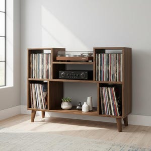 Può includere: Un mobile multimediale in legno scuro con quattro scomparti verticali pieni di dischi in vinile, un ripiano centrale con un giradischi e un amplificatore, e un ripiano inferiore aperto con una piccola pianta grassa e due vasi bianchi.