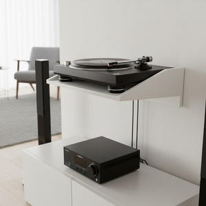 K&ouml;nnte beinhalten: Ein schwarzer Plattenspieler steht auf einem wei&szlig;en, an der Wand befestigten Regal. Darunter befindet sich ein schwarzer Stereo-Receiver auf einem wei&szlig;en Schrank. Hohe schwarze Lautsprecher flankieren das Setup und bilden ein modernes Audiosystem.