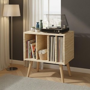 May include: A light-colored wood grain storage cabinet with four vertical compartments, supported by four tapered legs. The top surface holds a black record player with a clear lid, two small blue vases, and a small white succulent planter.