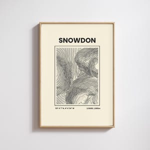 May include: A framed print displaying a topographic map of Snowdon. The print includes the name "SNOWDON" at the top, a black and white contour map, coordinates, and the height of 1,085m.