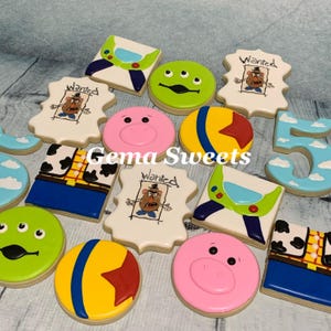 May include: Assortment of decorated sugar cookies featuring characters from the animated film Toy Story. Cookies include Buzz Lightyear, Mr. Potato Head, and the Little Green Men. The cookies are various shapes and colors, with the text "Wanted" on some.