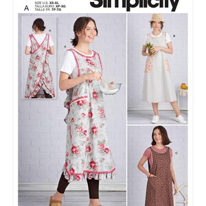 May include: Simplicity sewing pattern S9312 featuring three apron designs. View A shows a floral print apron with pink trim and ruffles. View B is a solid light-coloured apron with patterned pockets. View C is a dark brown apron with a small print.