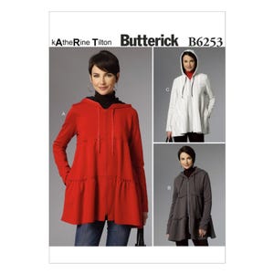 May include: A sewing pattern by Katherine Tilton for Butterick B6253. The pattern features a hooded jacket with a zipper closure and a tiered, ruffled hem. The image shows the jacket in red, white, and gray, with a model wearing each version.