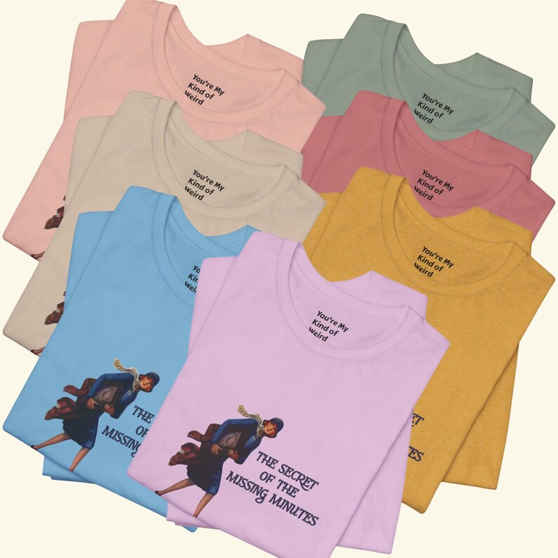 Op de afbeelding: Een collectie t-shirts met ronde hals in diverse kleuren, waaronder lichtblauw, roze, geel en beige. Elk shirt is voorzien van een afbeelding van een rennend persoon met een tas en de tekst "THE SECRET OF THE MISSING MINUTES" en "You're My Kind of Weird".