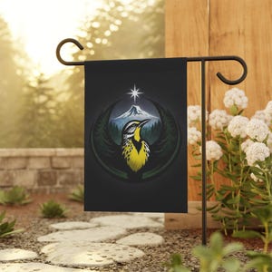 May include: A black garden flag featuring a stylized bird with yellow and black markings, set against a mountain and forest scene. A white star is above the mountain. The flag is displayed on a black metal stand in a garden setting.