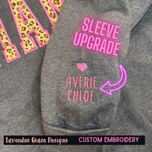 May include: Gray sweatshirt with a pink "SLEEVE UPGRADE" text and a pink heart with the names "AVERIE CHLOE" embroidered on the sleeve.  Lavender Grace Designs CUSTOM EMBROIDERY is printed on the bottom of the sweatshirt.