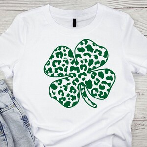 Pode incluir: Camiseta branca com um design de trevo de quatro folhas verde. O trevo &eacute; feito de um padr&atilde;o de estampa de leopardo.