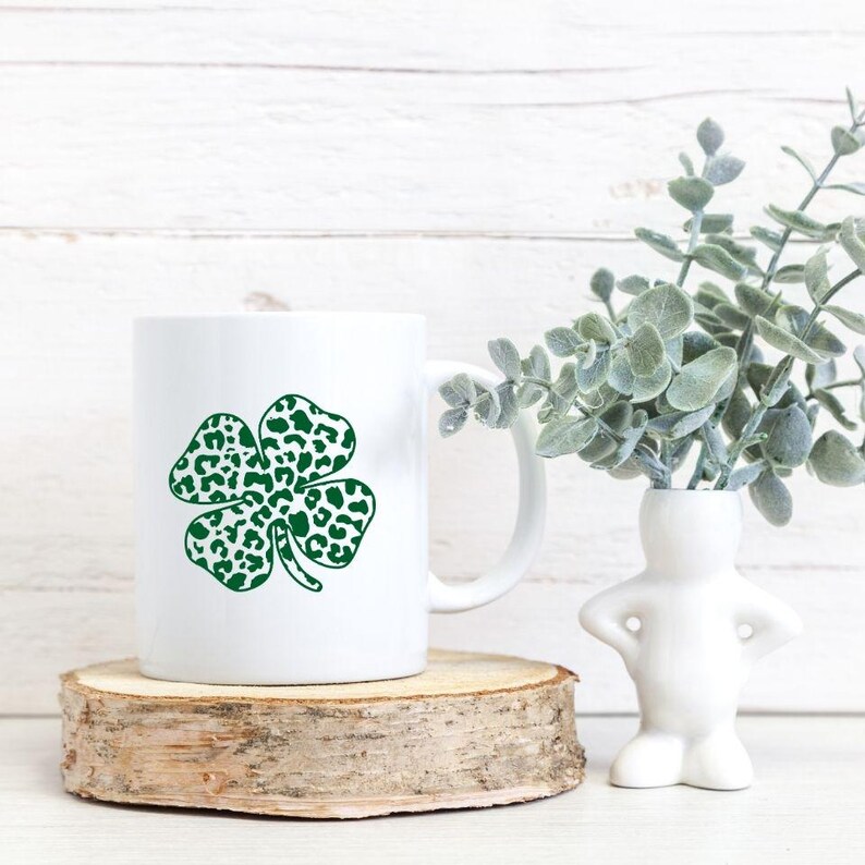 Pode incluir: Caneca de cer&acirc;mica branca com um design de trevo de quatro folhas verde. O trevo &eacute; estampado com manchas brancas, que se assemelham a uma estampa de leopardo.