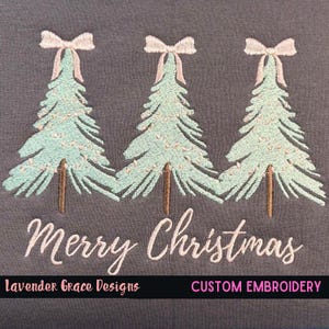 May include: Embroidered design featuring three Christmas trees with light blue needles, brown trunks, and pink bows. The text "Merry Christmas" is embroidered below the trees on a gray background.