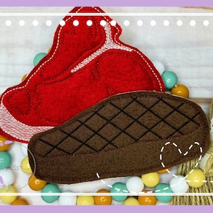 May include: Two felt patches shaped like a steak, one red and one brown with a diamond pattern. The patches are surrounded by colorful beads.