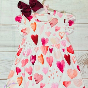 Vestido de seda color leche rojo y rosa con escote en forma de corazón y mangas onduladas. Vestido con estampado de corazones para niña pequeña. Tema de San Valentín.
