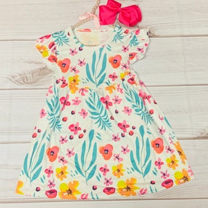 Puede incluir: Un vestido blanco con estampado floral con flores rosas, naranjas y amarillas y hojas verde azuladas. El vestido tiene mangas cortas con volantes y una falda fruncida.