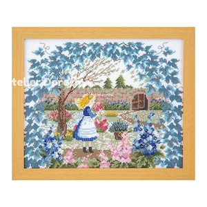 May include: Cross-stitch artwork in a wooden frame. The scene shows a young girl in a blue dress and blonde hair in a garden with flowers and a brick wall. The artwork is framed by blue foliage.