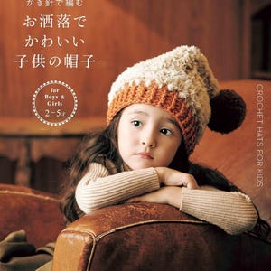 May include: A book cover titled "applemints" featuring a child wearing a two-toned crochet hat with a fluffy cream-colored top and a ribbed orange base, accented by a dark brown pom-pom. The text includes "かぎ針で編む お洒落でかわいい 子供の帽子" and "for Boys & Girls 2-5才".