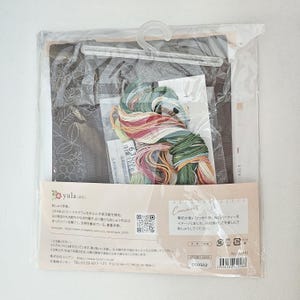 May include: A cross-stitch kit in a clear plastic bag. The kit includes a fabric with a floral design, embroidery floss in various colors, and instructions. The packaging features Japanese text and a QR code.