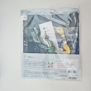 May include: A packaged embroidery kit featuring blue fabric with floral patterns, embroidery floss in shades of blue and yellow, and a needle. The kit includes instructions and a plastic hanger. The text on the package says "yula".