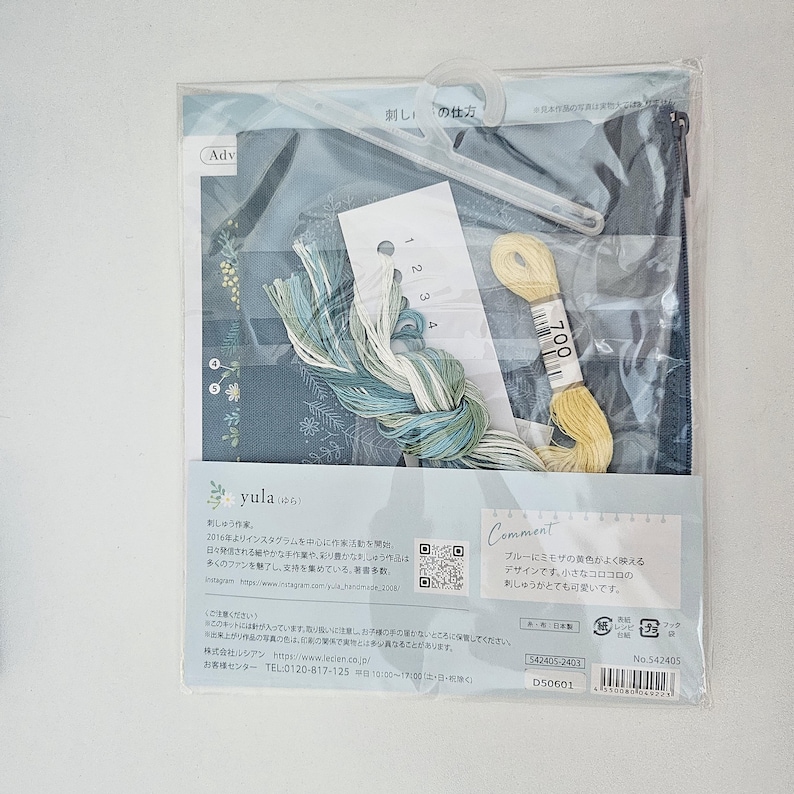 May include: A packaged embroidery kit featuring blue fabric with floral patterns, embroidery floss in shades of blue and yellow, and a needle. The kit includes instructions and a plastic hanger. The text on the package says "yula".
