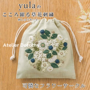 Puede incluir: Una bolsa verde claro con cordón y un diseño floral bordado. El bordado presenta flores blancas y azules, hojas verdes y el texto "yula" y "Atelier Dorothy". La bolsa tiene cordones blancos.