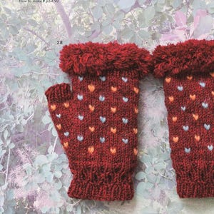 May include: A pair of fingerless gloves in a deep red knit featuring a pattern of small light blue and orange hearts. The gloves have a ribbed cuff at the wrist and a textured, fuzzy fringe trim at the top edge. The text 28 is visible.