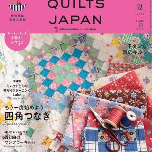 Puede incluir: La portada de una revista japonesa de acolchado, "QUILTS JAPAN", con fondo rosa y letras blancas. La imagen muestra patrones de edredones coloridos, muestras de tela, tijeras y carretes de hilo, enfocada en acolchado y patchwork.