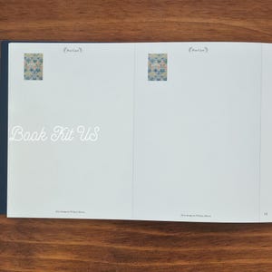 May include: Open book with the text "Book Kit US" in a cursive font. The book has two small floral design images and the words "Post Card" above them. The book is on a wooden surface.