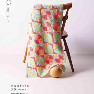 Puede incluir: Una colorida manta de ganchillo con un dise&ntilde;o de lunares en cuadrados rojos, rosas, azules y amarillos, colocada sobre una silla de madera. El dise&ntilde;o de la manta se destaca, mostrando la artesan&iacute;a hecha a mano.