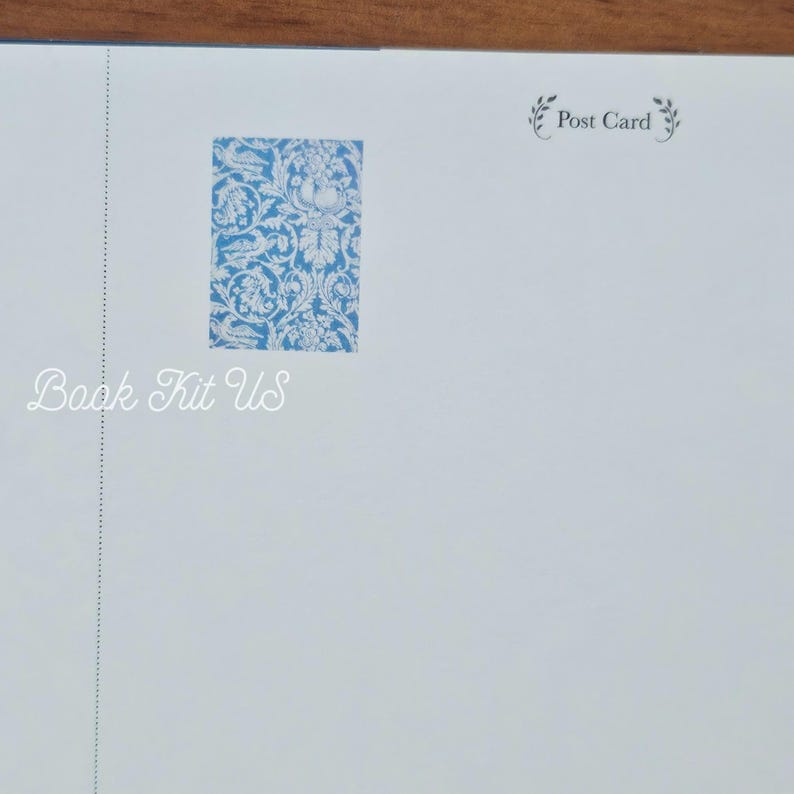 May include: A light blue postcard with a floral design in the upper center. The text "Book Kit US" is printed in a cursive font on the lower left. The words "Post Card" are printed on the upper right.