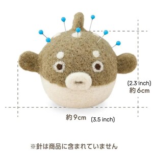 May include: A felt pufferfish pincushion, approximately 3.5 inches wide and 2.3 inches tall. The pincushion is tan and white with blue-tipped pins inserted. The text on the image says "The needles are not included."