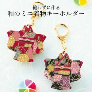 May include: Two miniature kimono keychains with gold-colored clasps. The kimonos are made of patterned fabric in shades of red, pink, and black, with gold accents. Japanese text is visible at the top of the image.