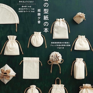 以下が含まれることがあります： 巾着の型紙の本というタイトルの書籍の表紙。オフホワイトの巾着袋やバッグが多数配置され、ベージュの紐が付いている。袋の形34点、袋口のデザイン14点、付属するパーツ16点などの日本語テキストが記載されており、背景はダークグリーンである。