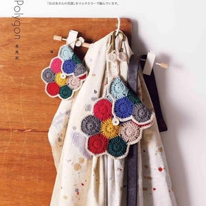 Puede incluir: Dos coloridos bolsos con forma de flor, hechos a ganchillo, colgados de una superficie de madera. Los bolsos est&aacute;n hechos de varios colores, incluyendo rojo, azul, amarillo y verde. El texto "Polygon" y texto japon&eacute;s son visibles.