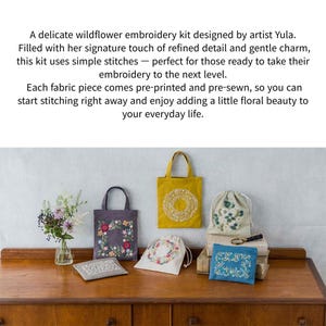 May include: A collection of embroidery kits featuring floral designs. The kits include tote bags, drawstring bags, and small pouches, all adorned with colorful embroidered flowers. The items are displayed on a wooden surface.