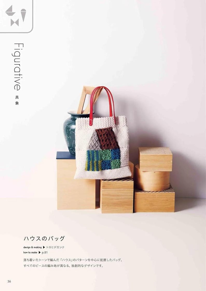 Puede incluir: Un bolso tote blanco con asas rojas presenta un dise&ntilde;o de casa de ganchillo en marr&oacute;n, azul y verde. La bolsa se exhibe sobre una pila de cajas de madera, con un jarr&oacute;n decorativo y un marco de madera en el fondo. La palabra "Figurative" est&aacute; impresa.