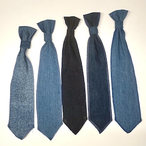 May include: Five denim ties in varying shades of blue and black are displayed against a white background. The ties are arranged vertically, showcasing their different textures and hues. Each tie has a knot at the top and a pointed bottom.