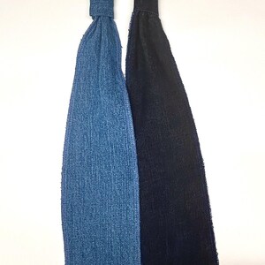 May include: Two neckties, one in denim blue and the other in black, are displayed against a white background. The ties are made of fabric and have a classic tie shape. The denim tie has a textured appearance, while the black tie has a smooth finish.