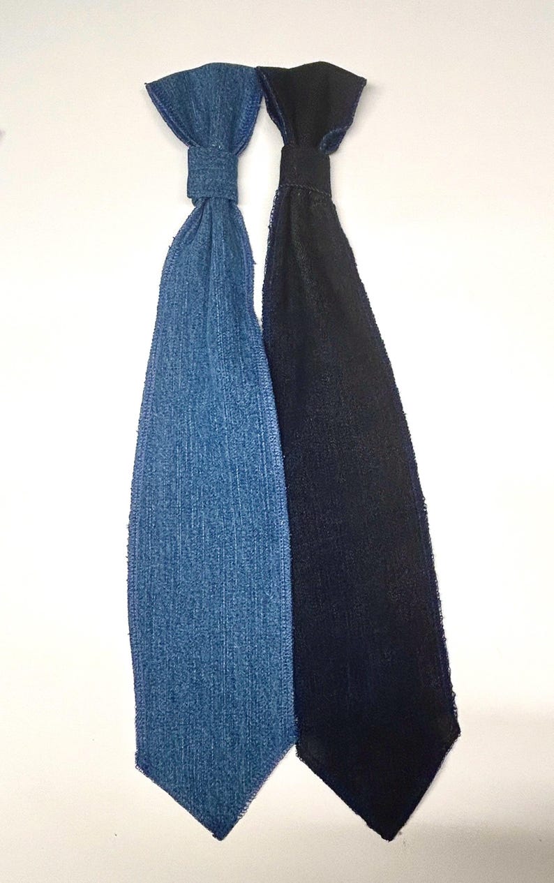 May include: Two neckties, one in denim blue and the other in black, are displayed against a white background. The ties are made of fabric and have a classic tie shape. The denim tie has a textured appearance, while the black tie has a smooth finish.