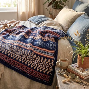 Op de afbeelding: Een rechthoekige gehaakte deken met een herhalend geometrisch patroon in marineblauw, crème en terracotta oranje. Het ontwerp bestaat uit horizontale banden met zigzag-, ruit- en kruismotieven, afgewerkt met een effen marineblauwe rand.