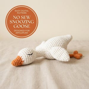 May include: A white crocheted amigurumi goose with an orange beak and feet, lying in a resting position with closed eyes. A circular graphic overlay contains the text: EASY DIGITAL PATTERN NO SEW SNOOZING GOOSE DESIGNED FOR AMIGURUMI.