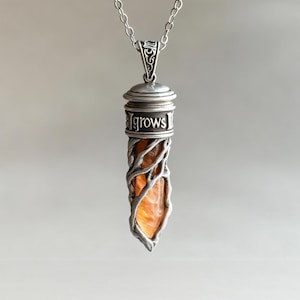 May include: A silver pendant necklace. The pendant has a cylindrical design with an orange stone encased in a silver wire frame. The word "grows" is inscribed on the silver top. The necklace hangs from a delicate silver chain.
